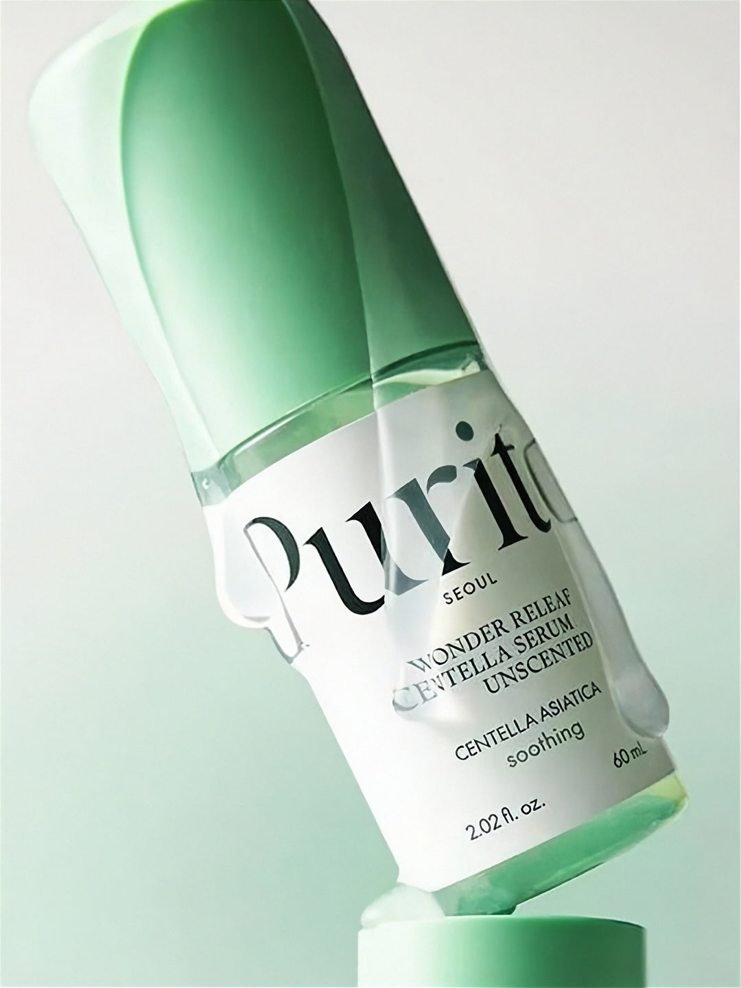 Tube of Purito Wonder Releaf Centella Serum Unscented cover in clear liquid, tilted sideways on a gradient light green background.