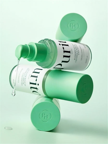 Green bottles of Purito Wonder Releaf Centella Serum Unscented stacked on one another with liquid coming out of one pump, on a light green background
