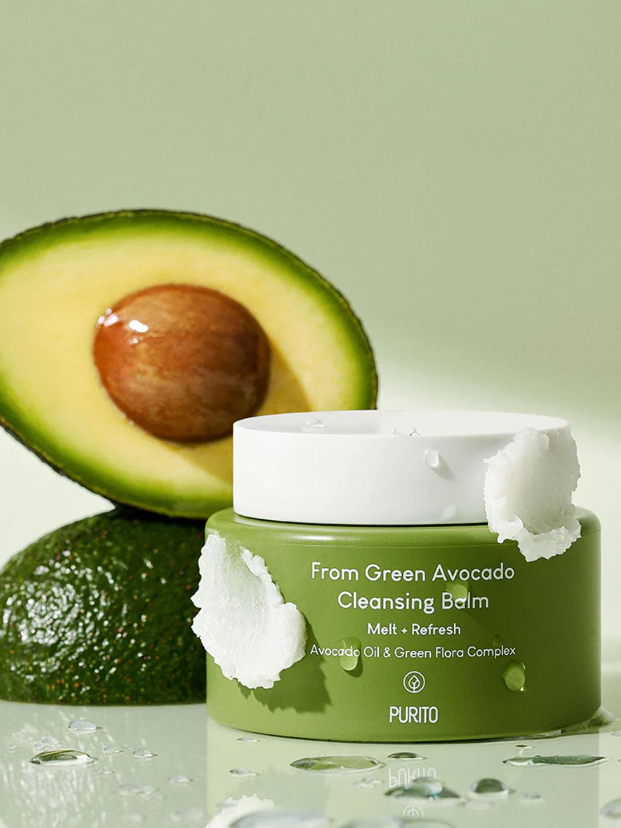 PURITO From Green Avocado Cleansing Balm in a green jar with a white lid, styled with a halved avocado and a whole avocado on a light green background.