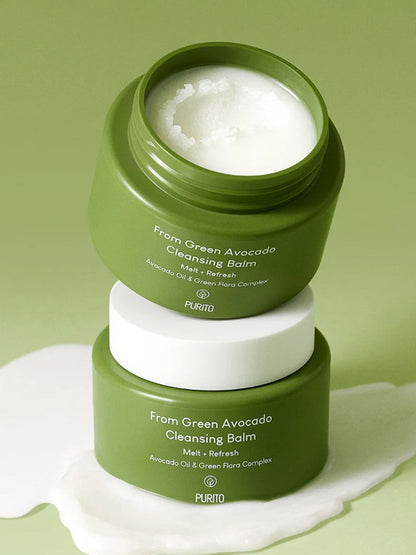 Two green PURITO jars of From Green Avocado Cleansing Balm stacked on a light green background, with one jar open to show the white balm inside and a white cream spill in front.