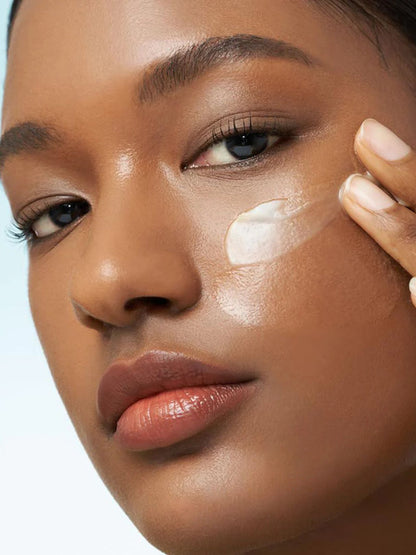Close-up of a woman applying Purito From Green Avocado Cleansing Balm to her cheek, showing a smooth, glossy skin texture against a light blue background.
