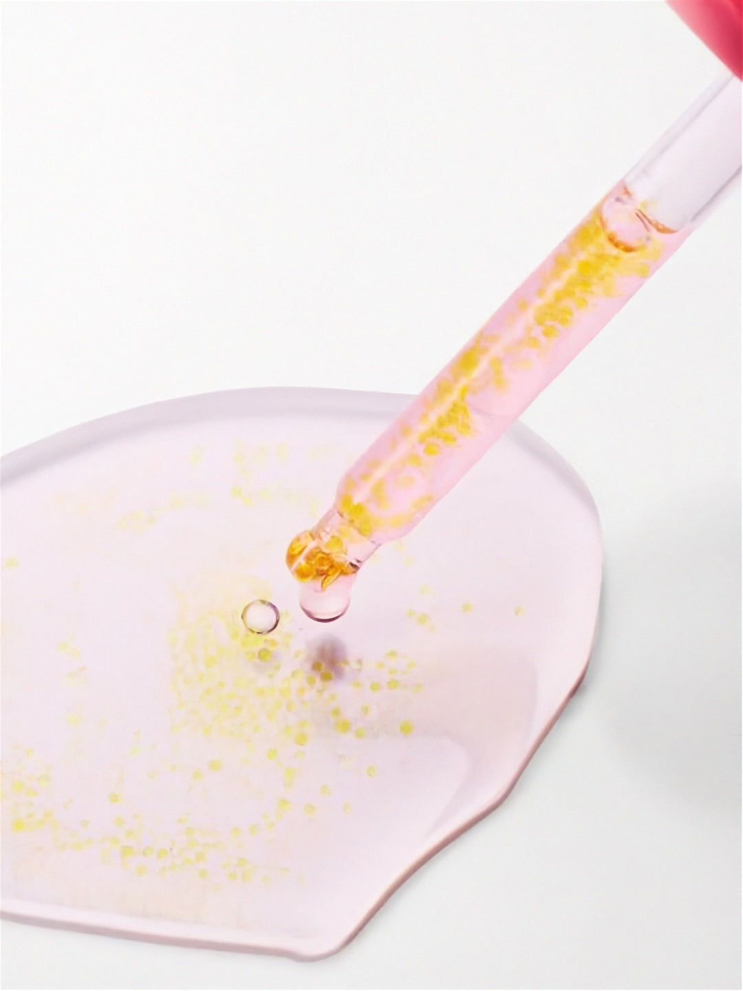 Close up of dropper from Purito Seoul TXA 6 Niacinamide 10 Retinal Serum with a light pink puddle of serum showing the encapsulated retinal beads, on a white background