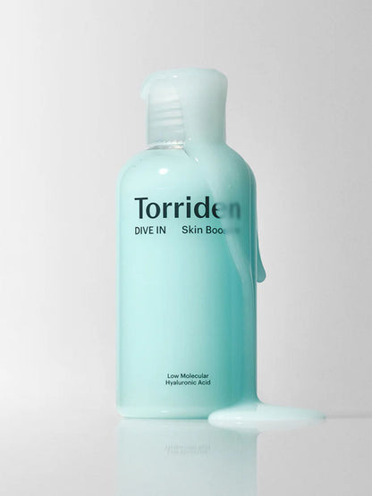 A bottle of Torriden Dive In Skin Booster with some of the product shown dripping from the bottle onto a reflective white surface against a light gray background.