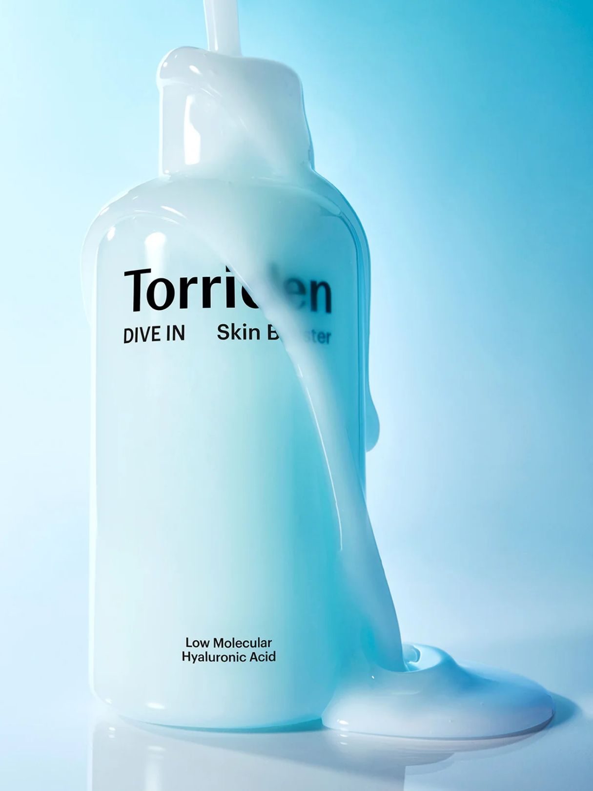 A bottle of Torriden Dive In Skin Booster with thick, glossy white liquid dripping from the top and pooling around the base, set against a soft light blue gradient background.