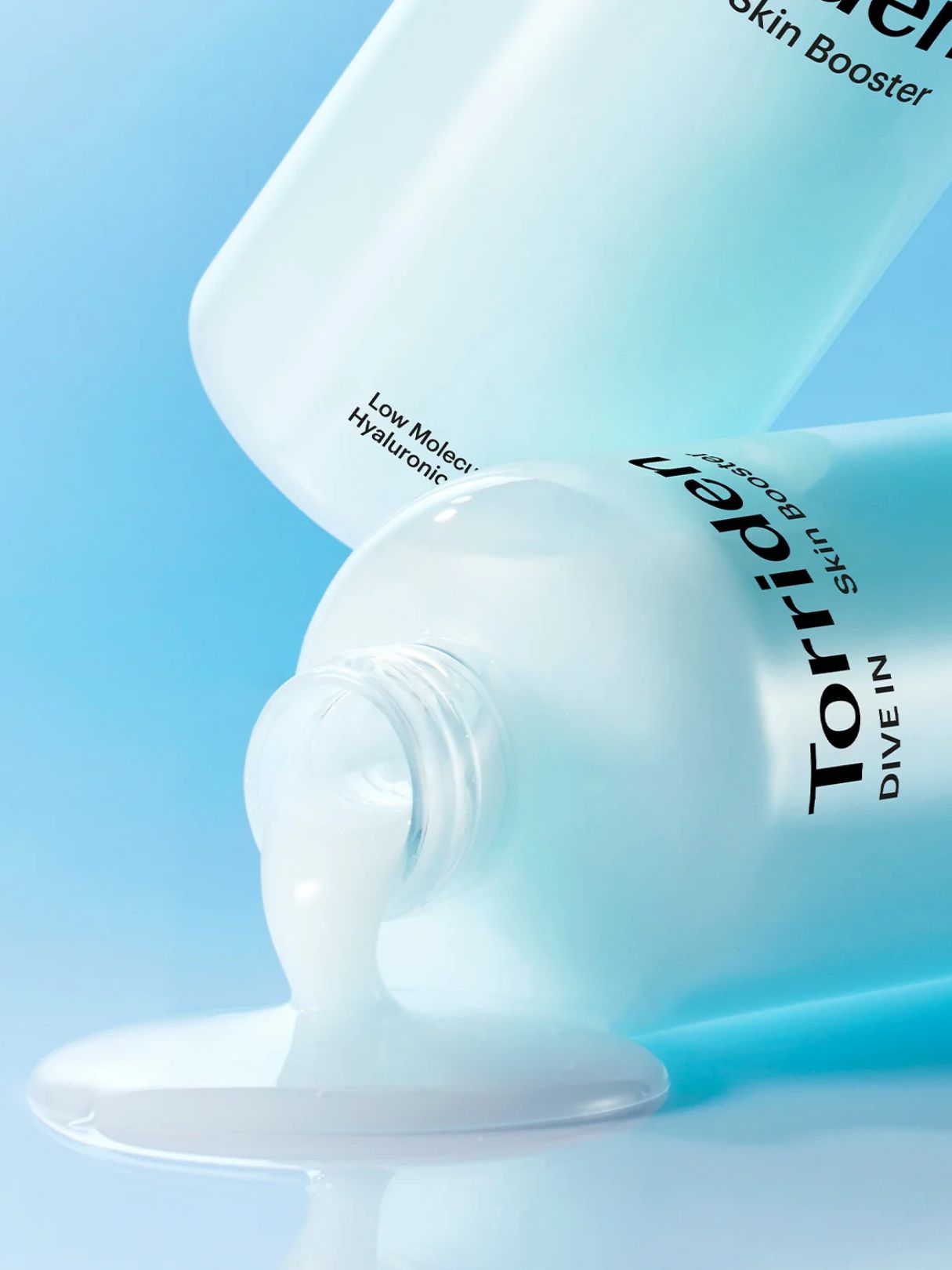 Two bottles of Torriden Dive In Skin Booster spilling onto a glossy surface against a soft light blue background. 