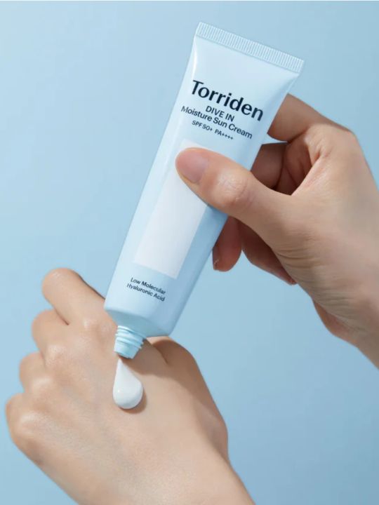Hand holding a tube of Torriden Dive In Moisture Sun Cream against a light blue background