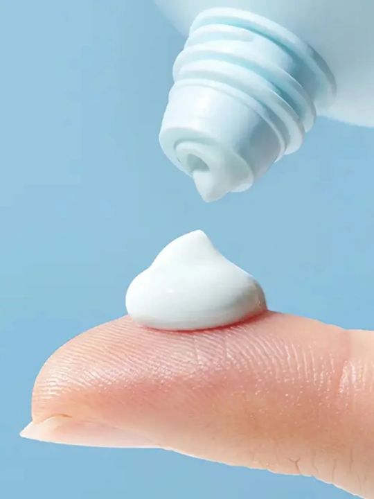 Close-up of a  a small amount of Torriden Dive In Moisture Sun Cream on a finger tip with a blue background