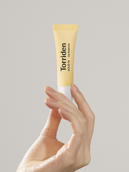 Woman's hand holding up a tube of Torriden Solid In Lip Essence, against a light grey background. Available at Sinless Skincare.