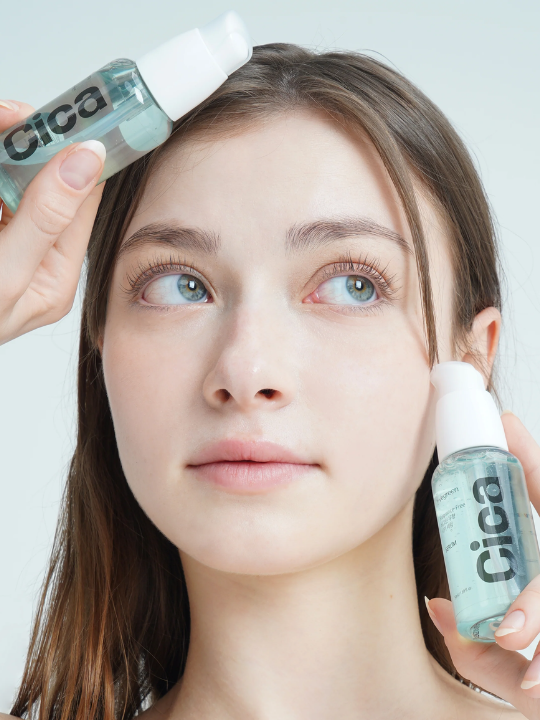 Woman holding two bottles of Vegreen fragrance-free cica serum to her face.
