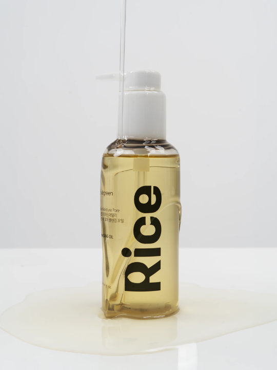 Vegreen Rice Cleansing Oil with liquid pouring over the bottle creating a puddle, against a white background. Available at Sinless Skincare Swizerland.