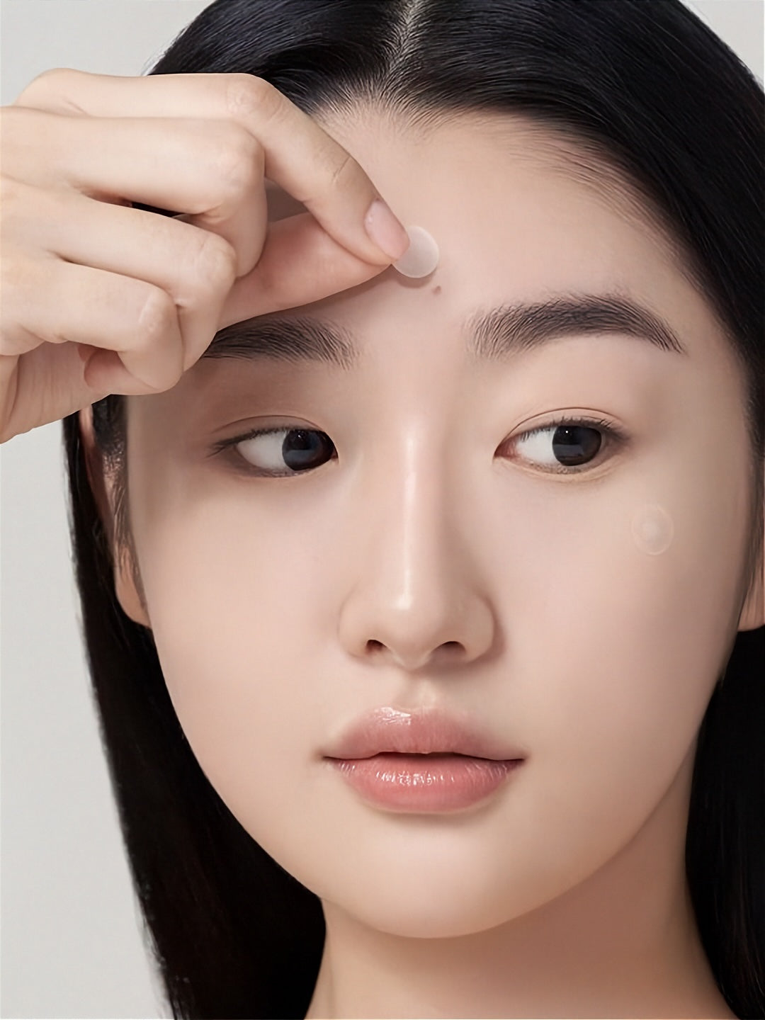 Woman applying a Purito Wonder Releaf Centella Spot Patch to her forehead