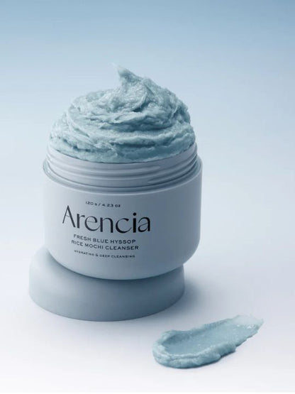 Open jar of Arencia Blue Hyssop Rice Mochi Cleanser with swatch on a light blue background