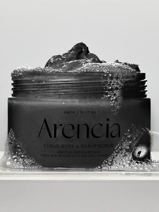 A jar of Arencia Cloud Body & Scalp Scrub  (Black Tea & Yuzu) with dark scrub visible at the top, surrounded by foam bubbles on a light gray background.
