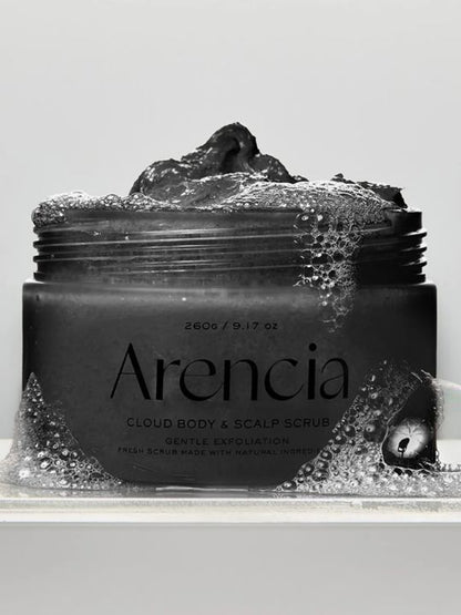 A jar of Arencia Cloud Body & Scalp Scrub  (Black Tea & Yuzu) with dark scrub visible at the top, surrounded by foam bubbles on a light gray background.