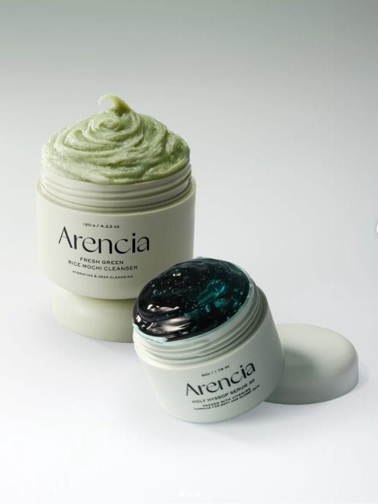 Open jars of Arencia's Holy Hyssop Serum 30 and Fresh Green Rice Mochi Cleanser on a light grey gradiant background