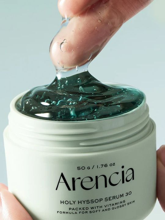 Arencia Holy Hyssop Serum 30 jar with a finger dipping into the serum, on a light green background.