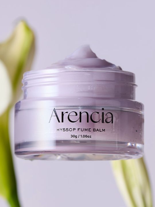 Open jar of Arencia Hyssop Fume Balm on a light purple background with botanical elements