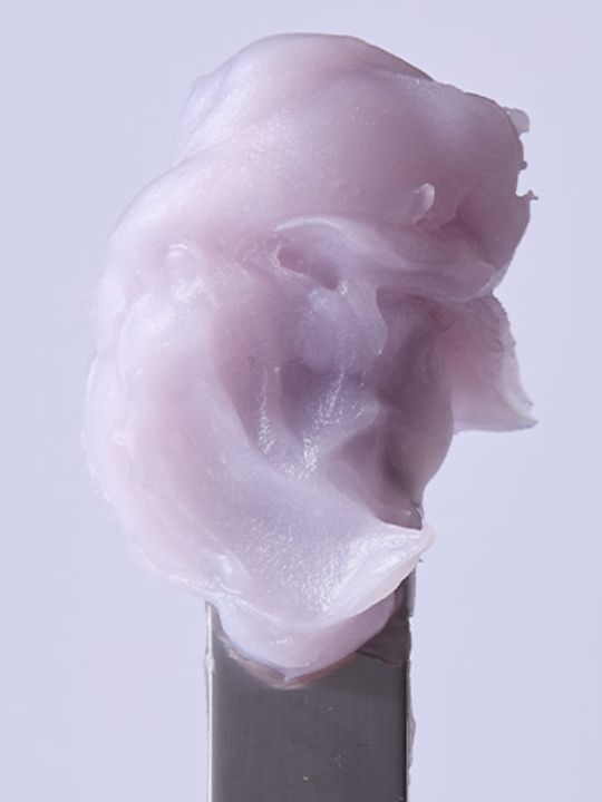 Close-up of Arencia Hyssop Fume Balm cream on spatula against light purple background