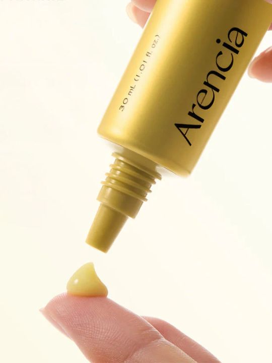 Arencia Retinal Booster Shot applicator and yellow cream on a finger against a white background