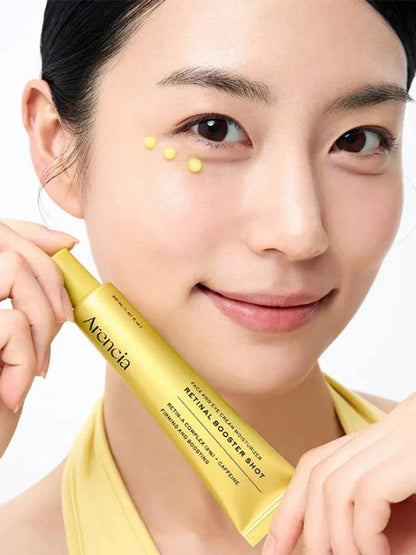 Woman holding a tube of Arencia Retinal Booster Shot with yellow cream under her eye