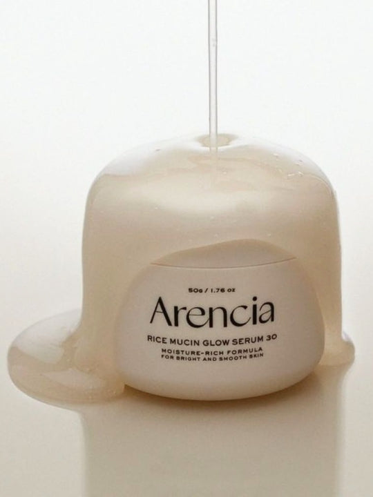 Jar of Arencia Rice Mucin Glow Serum 30 with a liquid being poured onto it, set against a clean white background.