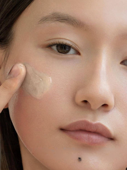 Close-up of a person applying a translucent beige gel to their cheek with a finger.