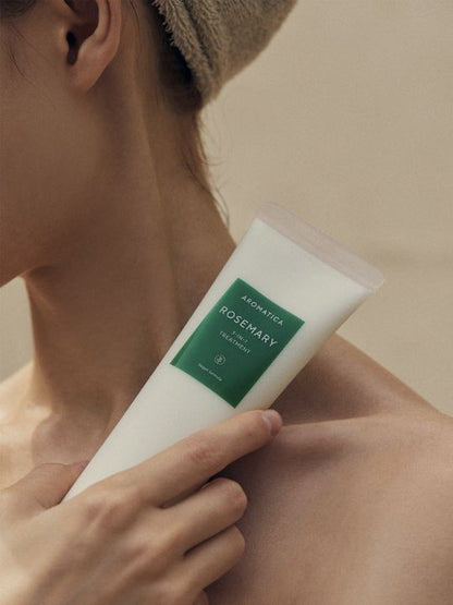 Woman holding a tube of Aromatica Rosemary 3 in 1 Treatment to her neck against a neutral background