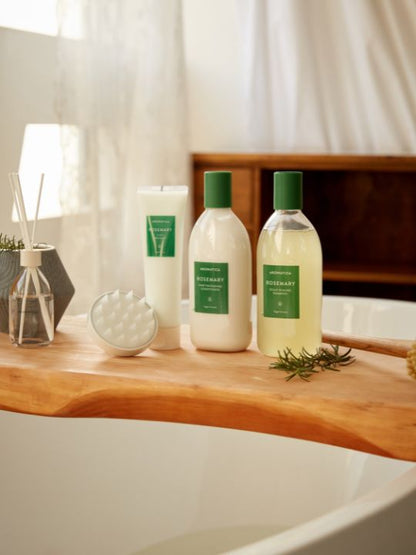 Three products from Aromatica's Rosemary hair care line on a wooden shelf with a bathtub in the background.