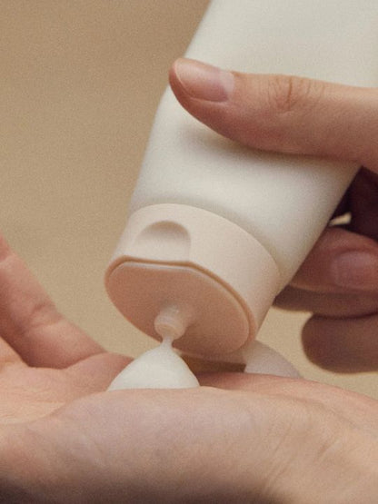 Close-up of a hand holding a tube of Aromatica Rosemary 3 in 1 Treatment against a beige background