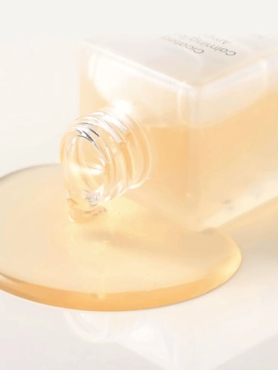 Close up of Dewdap Cicatea Calming Repair Ampoule tipped over with serum pouring out, on a white surface