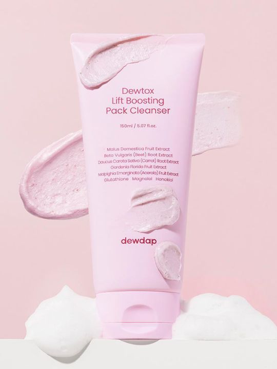 Tube of Dewdap's Dewtox Lift Boosting Pack Cleanser with patches of cream smeared on top, sitting on white foam, against a light pink background