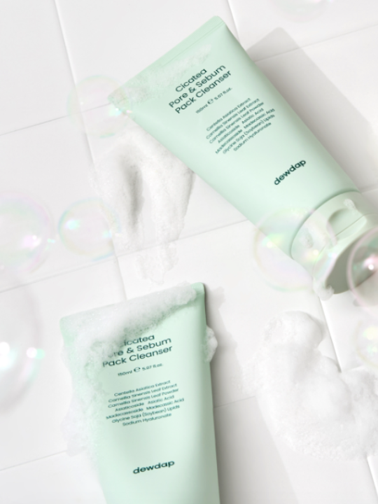 Two bottles of Dewdap Cicatea Pore & Sebum Pack Cleansers on a white tiled surface, surrounded by white foam.