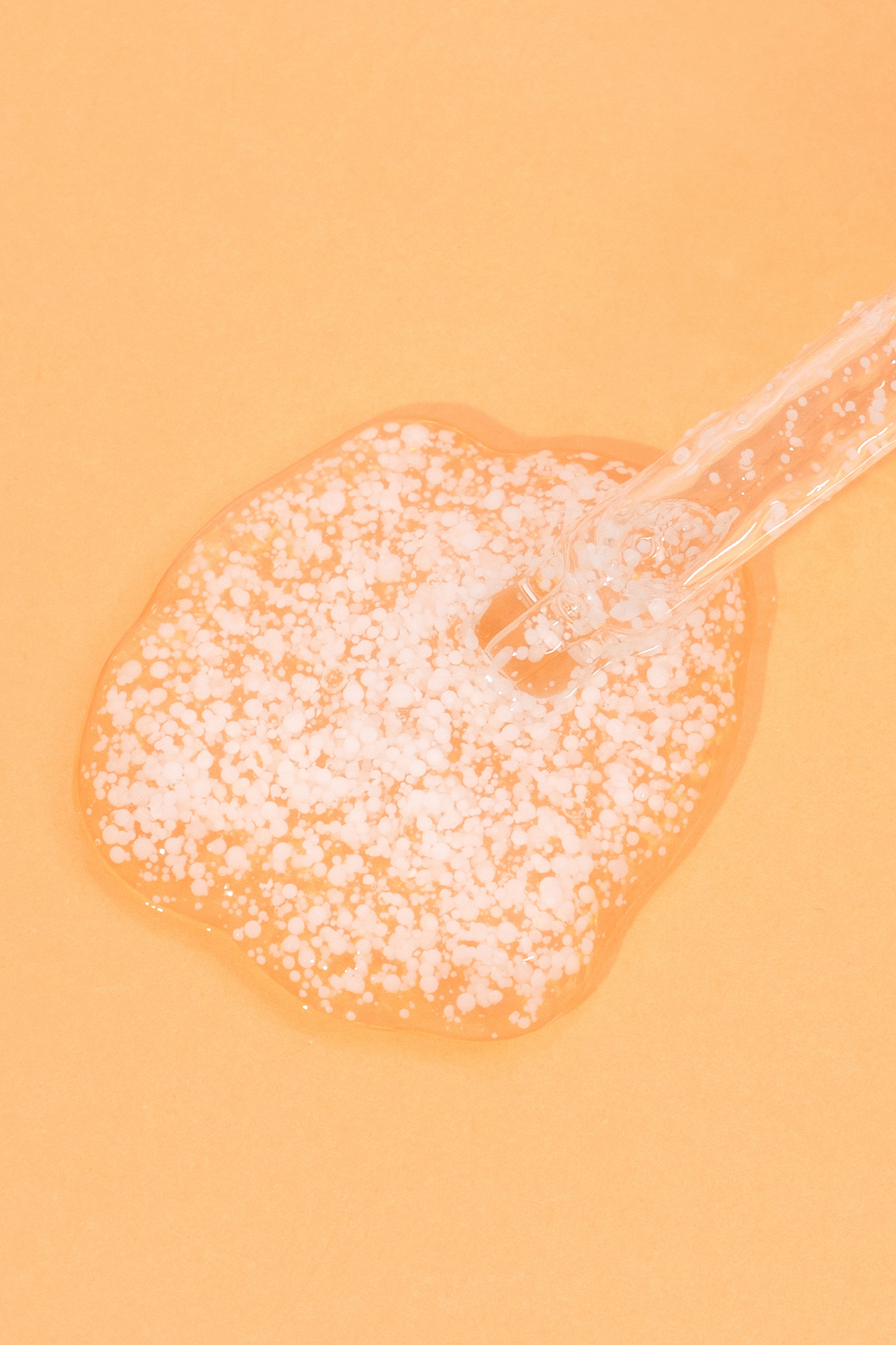 Texture shot of Meisani's Glow Drops Vitamin C Serum with the dropper visible, against a light orange background.