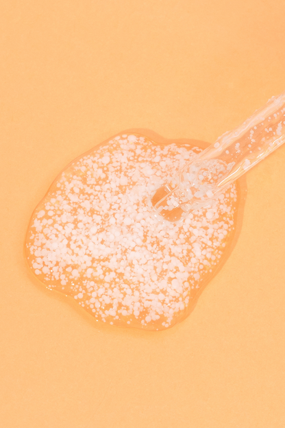 Texture shot of Meisani's Glow Drops Vitamin C Serum with the dropper visible, against a light orange background.