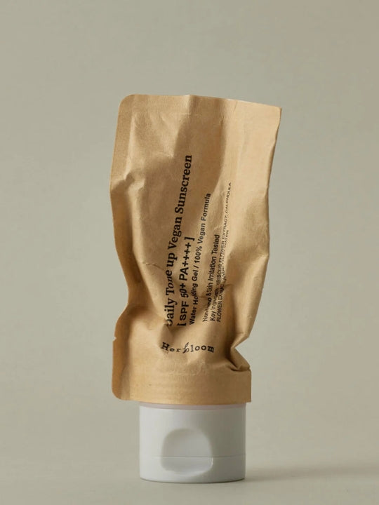 A crinkled kraft paper pouch of Herbloom Daily Tone Up Vegan Sunscreen SPF 50+ with a white flip-top cap, set against a solid light gray background.