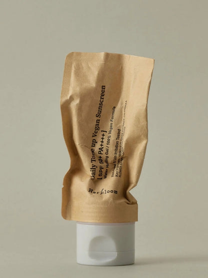 A crinkled kraft paper pouch of Herbloom Daily Tone Up Vegan Sunscreen SPF 50+ with a white flip-top cap, set against a solid light gray background.