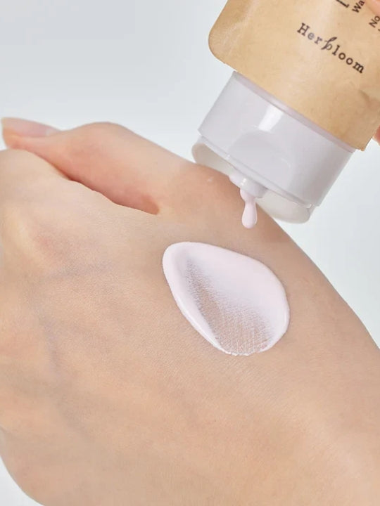 A close-up of a hand receiving a dollop of pale pink cosmetic cream from a tube of Herbloom Daily Tone Up Vegan Sunscreen SPF 50+