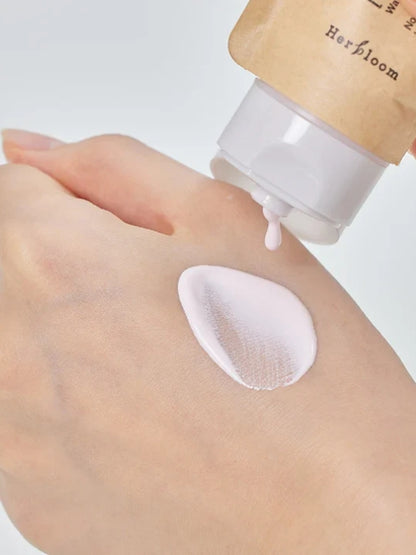 A close-up of a hand receiving a dollop of pale pink cosmetic cream from a tube of Herbloom Daily Tone Up Vegan Sunscreen SPF 50+
