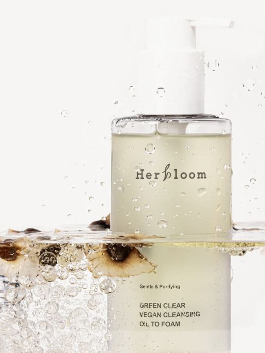 Herbloom Green Clear Cleansing Oil to Foam bottle submerged in clear water with botanical elements against a white background