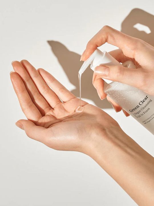 Person holding a bottle of Herbloom's Green Clear Cleansing Oil to Foam and pumping it onto their palm against a neutral background