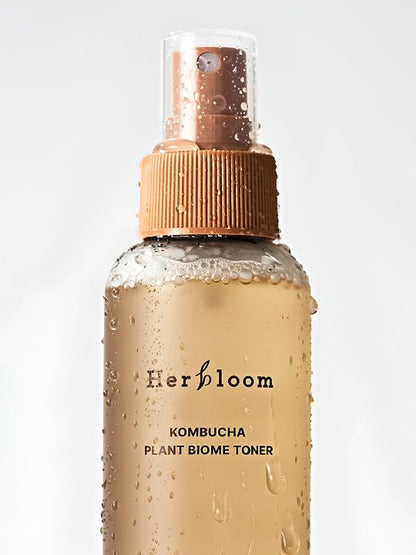 Close up of spray bottle with words Herbloom Kombucha Plant Biome Toner and water droplets, against a white background