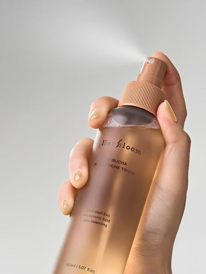 Close up of a hand spraying a bottle of Herbloom Kombucha Plant Biome Toner against a grey background