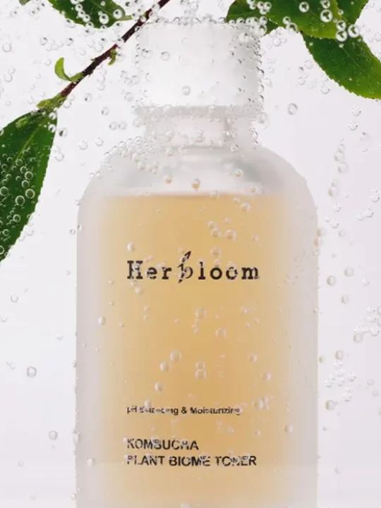 Herbloom Kombucha Plant Biome Toner with water droplets and green leaves on a white background