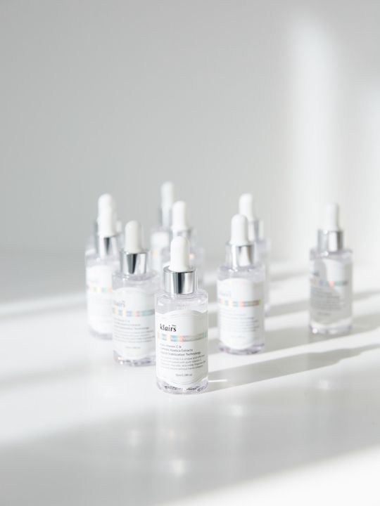 Set of Klairs Freshly Juiced Vitamin Drop bottles with shadows on a light grey surface and background