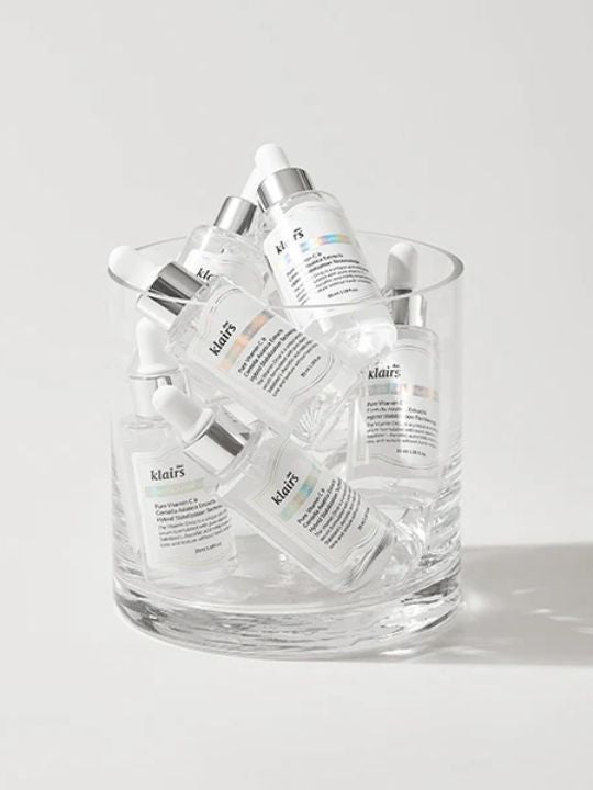Glass container filled with bottles of Klairs Freshly Juiced Vitamin Drop on a light grey background