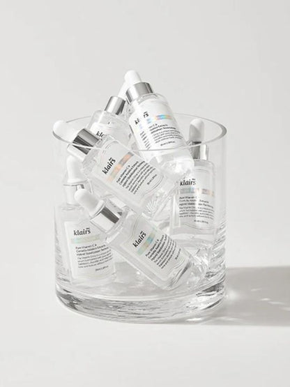 Glass container filled with bottles of Klairs Freshly Juiced Vitamin Drop on a light grey background