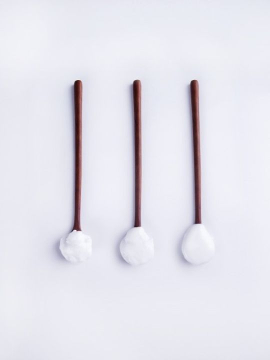 Three spoons with brown handles and white cream on a white background