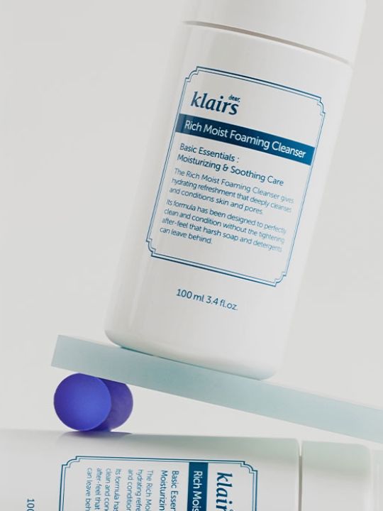 Klairs Rich Moist Foaming Cleanser standing on a slanted surface on a white background