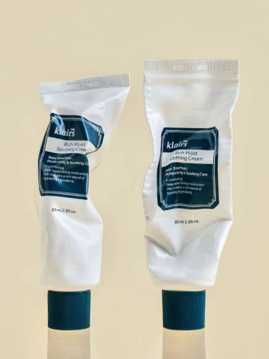 Two white tubes of Klairs Rich Moist Soothing Cream crumbled up on a beige background