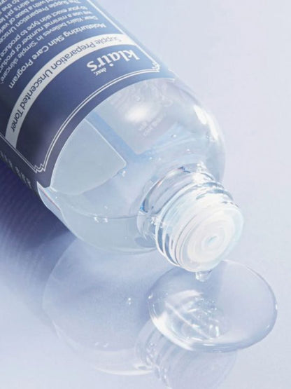 Klairs Supple Preparation Toner Unscented bottle tipped over without cap and with liquid pouring out, on a light grey background